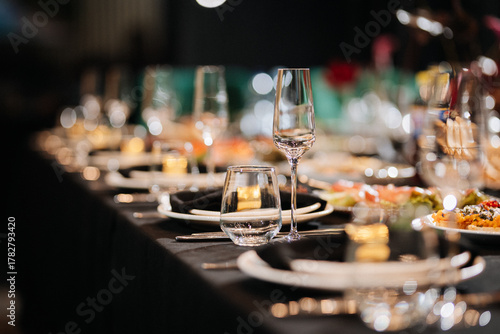 Closeup of elegant banquet table with glasses and black napkins in soft bokeh light