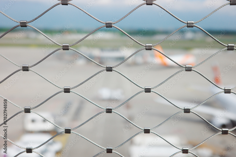 Fototapeta premium Metal security mesh fence with blurred airport runway background