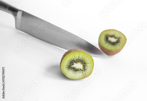 Un kiwi cortado por la mitad junto a un cuchillo, sobre un fondo blanco