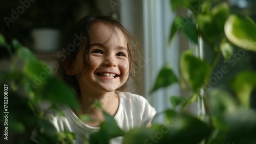 Wallpaper Mural Joyful little girl laughing while watering plants indoors, natural sunlight through window, cozy home environment, happiness and curiosity, playful child Torontodigital.ca