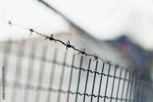 Barbed wire line above metal fence used for property safety and perimeter separation, concept of restricted access, protection and construction site boundary in industrial environments