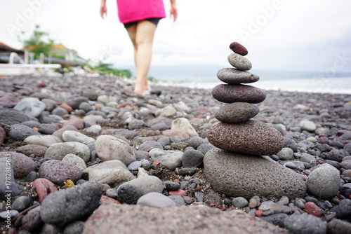 Stone balance with blur woman wearing pink shirt walking alone with barefoot from behind on the beach. Inspirational and spiritual concept background. Peace, harmony and abundance concepts.