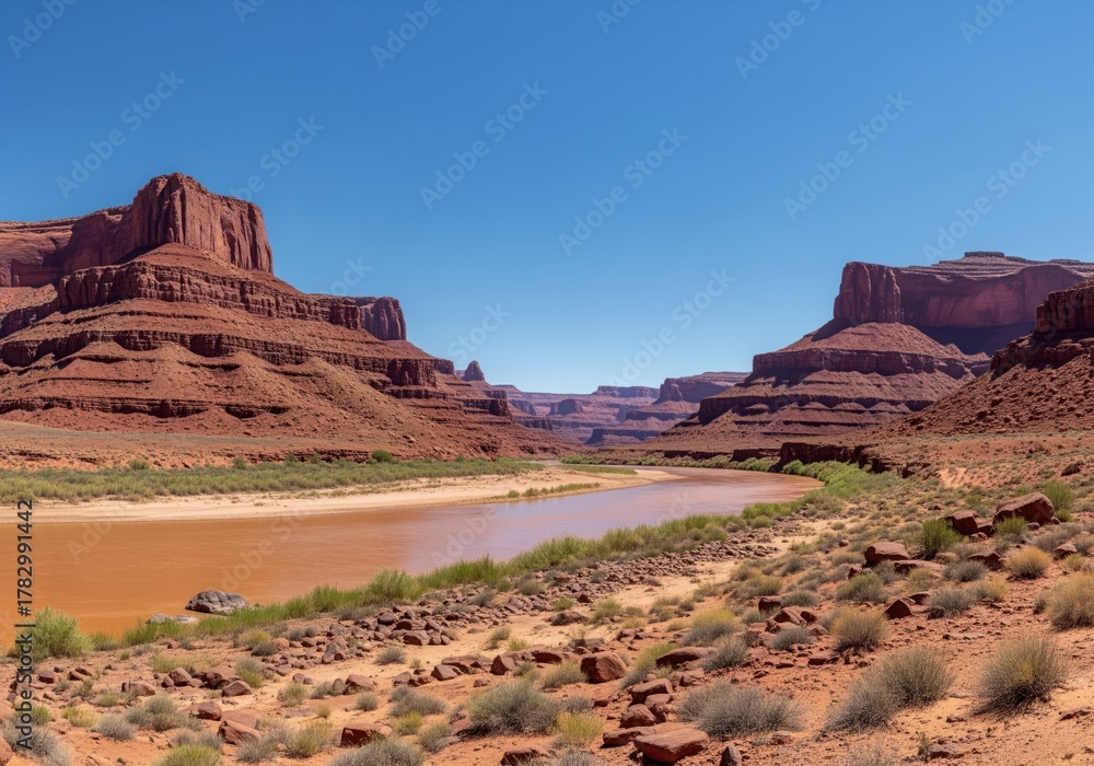 Obraz premium Panoramic view of a muddy river flowing through massive red rock canyons under a clear blue sky.