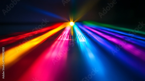 A cube is sitting on a table in front of a colorful background. The cube is made of glass and is reflecting the colorful lights in the background