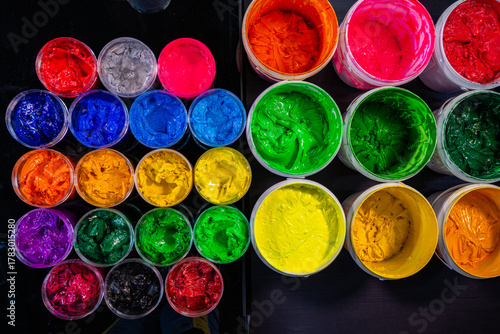 A collection of plastisol inks stored in sturdy barrels and glass jars, each filled with rich and vibrant colors red, blue, yellow, green, pink, orange, purple, and white in screen printing factory