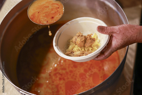 Volunteer hand serving hot soup from large pot with ladle. food donation showing charity and help for poverty, compassionate and warm meal for community