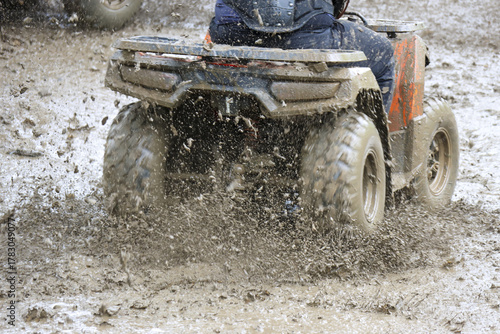 Exciting action of an ATV quad driving through mud. An off road adventure creating big splash with powerful wheel during an extreme motorsport race in dirt