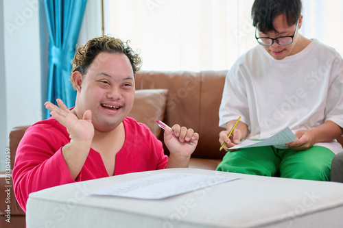 A man with down syndrome are engaging in an activity, displaying happiness and focus. One individual is smiling and waving, while the other is concentrating on writing
