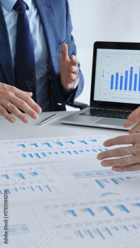 Business people collaborating at a table, discussing financial data and reports with a calculator and laptop displaying charts, focusing on strategy and planning, close up vertical view
