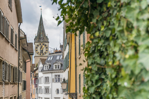 European old town street with historic clock tower, colorful buildings, and green foliage. Charming architecture showing traditional houses and church spire in scenic village.Zurich oldtown.