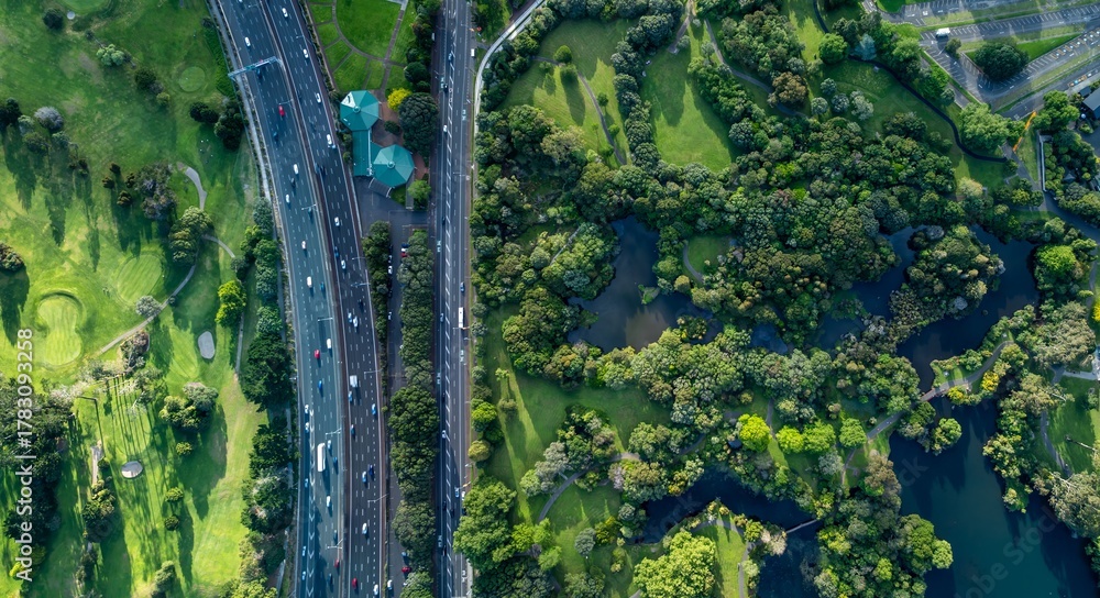 Obraz premium Aerial view of Western Springs Park, New Zealand, showcasing the juxtaposition of urban infrastructure and natural beauty. A busy highway runs alongside lush parkland.