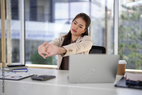 Asian woman professional worker takes vital break office desk stretch wrist relieve fatigue improve focus boost productivity during demanding work day