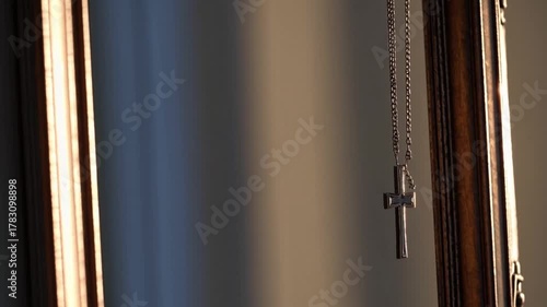 Silver cross necklace hanging in reflective frame during soft afternoon light indoors