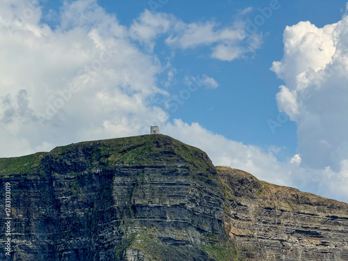 Stone tower atop dramatic sea cliffs under a blue sky with clouds