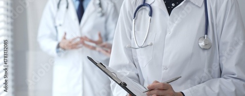 A medical professional with a stethoscope writes on a clipboard while a doctor and female assistant collaborate in a clinic, discussing patient data and healthcare information
