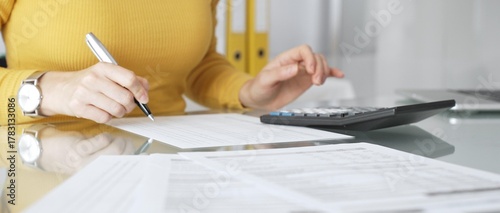 Woman calculating finance, taxes, and accounting paperwork at office desk, budgeting expenses, filing documents. Audit and taxes in business