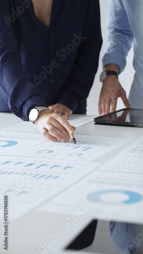 Professional team reviewing financial documents, pointing at charts on desk, collaborating to analyze data and strategize business growth. Business people concept