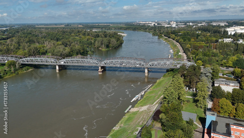 Fototapeta Naklejka Na Ścianę i Meble -  Panoramic Aerial Drone View Capturing the Po River Flowing Through Cremona Lombardy with a Bridge and Lush Greenery Under a Clear Blue Sky