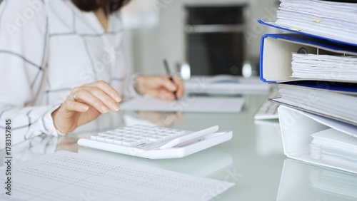 Quadro su tela Woman working in office, calculating finances with white calculator, managing accounting paperwork and business expenses