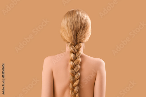 Beautiful young woman with pigtail hairstyle and naked back on beige background
