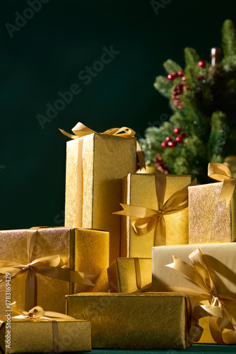 Golden Christmas presents with ribbons beside pine tree on dark green background, festive still life for winter holiday celebration scene.