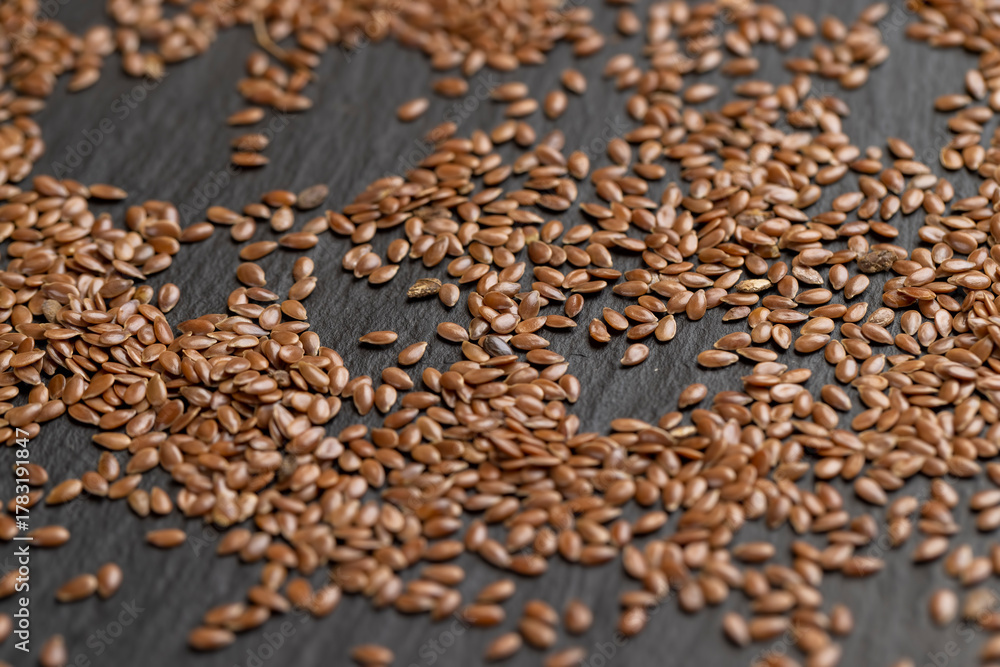 Obraz premium flax seeds scattered on slate, light brown flax seeds scattered on black slate surface
