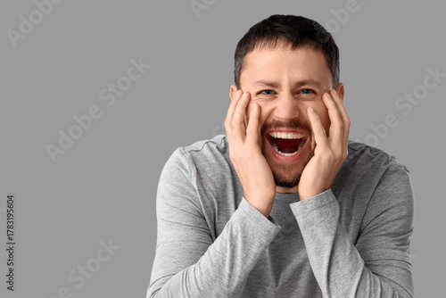 Young man screaming on grey...