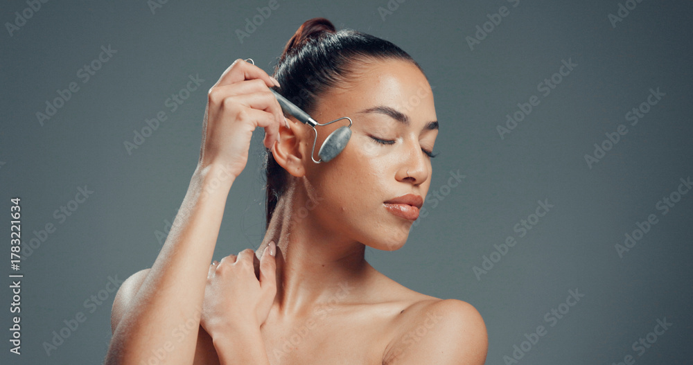 Obraz premium Beauty, woman and jade roller in studio with massage for skincare, dermatology and facial tension. Relax, person and cosmetic tool for lymphatic drainage, wellness or mockup space on gray background.