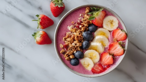 Healthy smoothie bowl with banana, strawberry, blueberry and granola on marble background