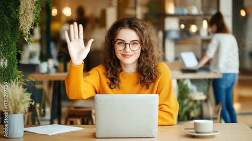 Enthusiastic greeting at Cafe: A young, cheerful individual wearing glasses, extends a warm, friendly wave at a cafe. The soft light of cafe highlights their amiable nature.