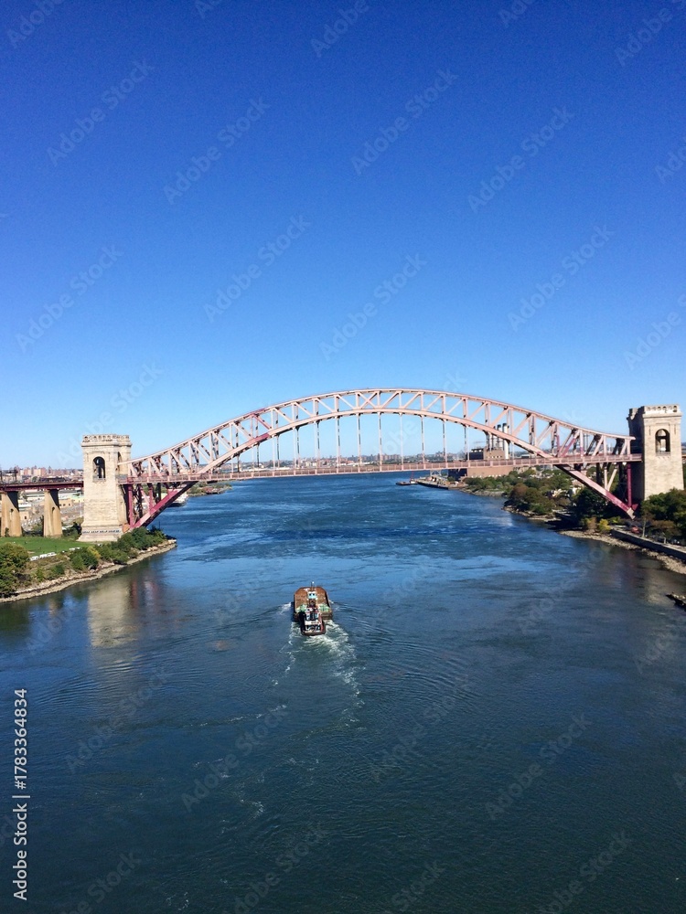 Naklejka premium Majestic Steel Arch Bridge Spanning River under Clear Blue Sky with Passing Boat