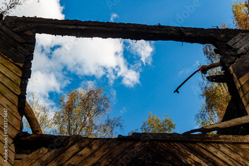 Upward view through charred timber framing a crisp blue sky with white clouds, a poignant scene of fire's ruin and nature's persistent hope