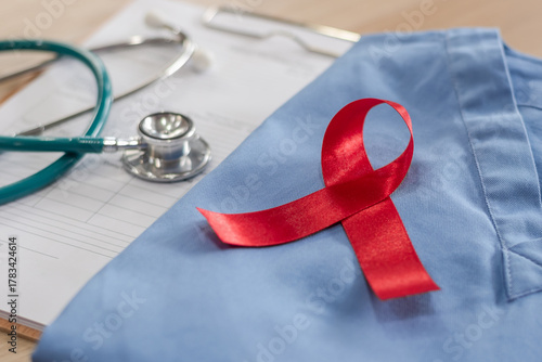 World aids day and national HIV AIDS and ageing awareness month concept with red ribbon on medical or surgical doctor's lab uniform on work desk in hospital background