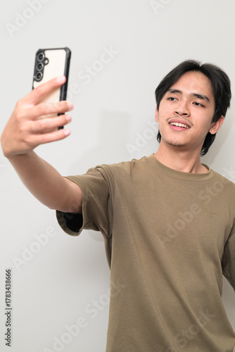 Portrait of handsome young Asian Thai man using phone taking selfie against white background
