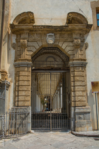 An ornate arched stone gate in the Kalsa district of Palermo in Sicily, Italy. The Baroque arch is flanked by rusticated pilasters supporting a richly decorated entablature comprising architrave