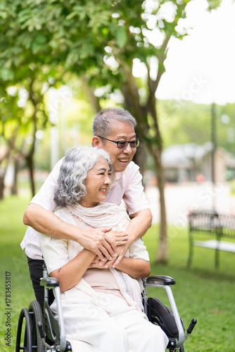 Senior woman in wheelchair walking with old man in park. Elderly family couple. man supporting taking care of paralyzed woman in chair for people with disability outdoor. Rehabilitation.