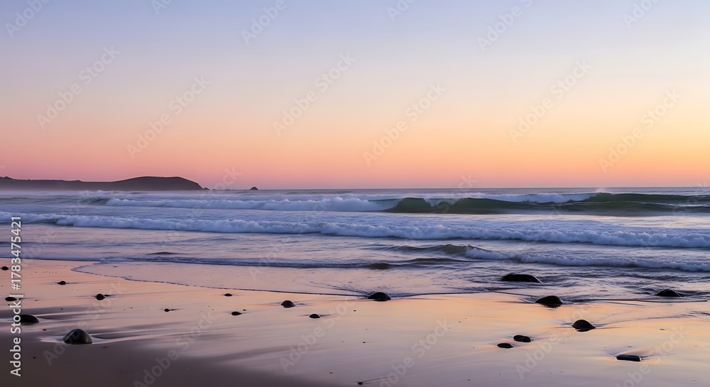 Obraz premium Gentle ocean waves under a soft, pastel sunset sky at a rocky beach