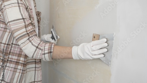 Unknown female construction worker wearing protective gloves applying plaster, smoothing wall surface during home renovation work