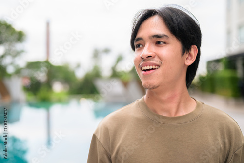 Portrait of handsome Young Asian Thai man outdoors next to swimming pool during summer