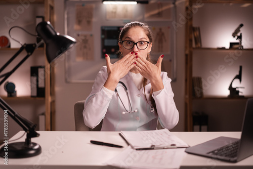 Shocked amazed young woman physician working in medical clinic. surprised doctor woman in white coat showing shock gesture while working on night shift in hospital.