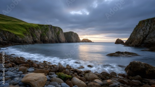 Rugged cliffs embrace a serene cove with waves lapping a pebble shore at twilight