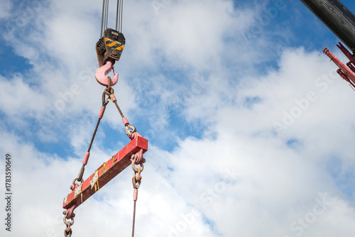 Bild auf Leinwand Crane machinery is lifting heavy object using the spreader bar on cloudy sky background