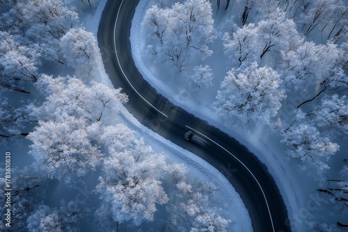 A winding road snakes through a winter wonderland, showcasing frosted trees and a car in motion.  A high-angle, serene view captures the tranquil beauty of a snowy landscape.