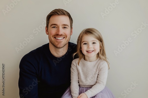 A joyful father and daughter pose for a portrait, showcasing warm smiles and a close family bond against a neutral backdrop.