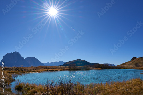 Lake Iman or Lech da Iman, a little mountain lake in alpine meadows of Puez-Odle Nature Park in Dolomites. An ideal rest area in a popular hiking to Seceda mount. Rays radiating from the sun.