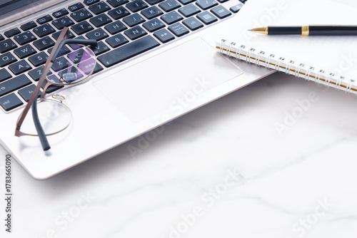 ノートにメモをとりながらノートパソコンでデスクワークをしているイメージ
