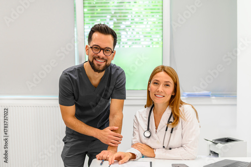 Portrait of smiling male and female doctor colleagues collaborating at desk in hospital during clinical work