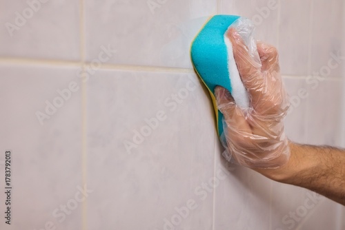 Wallpaper Mural A Man Diligently Cleaning a Tiled Bathroom Wall with His Gloves and a Scrubber Tool Torontodigital.ca
