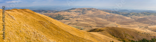 Rolling dry golden hills and a distant valley, bathed in warm light during golden hour, creating a scenic nature panorama