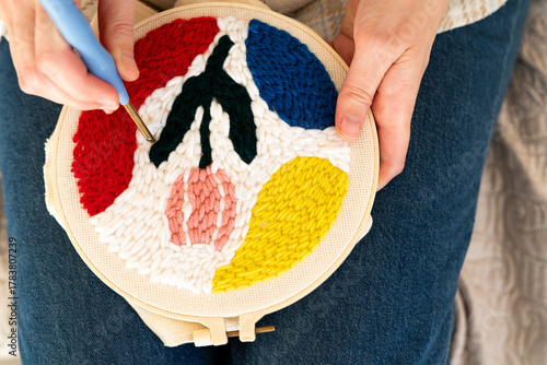 woman knitting wool. A person uses a hook to craft a colorful textile design. Bright yarn forms flowers and shapes in various colors. This creative activity takes place in a warm, inviting room.